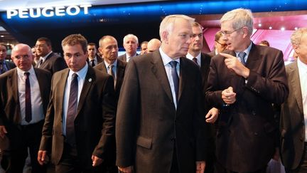 Le Premier ministre, Jean-Marc Ayrault (au c.), et le pr&eacute;sident du directoire de PSA, Philippe Varin (&agrave; dr.), sur le stand du constructeur install&eacute; au Mondial de l'automobile &agrave; Paris, le 8 octobre 2012. (THOMAS SAMSON / AFP)