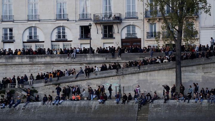 Des personnes regardent l'incendie de la cathédrale Notre-Dame depuis les rives de la Seine, le 15 avril 2019. (THOMAS SAMSON / AFP)