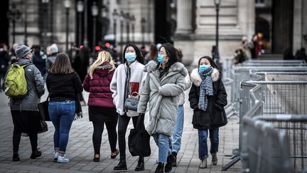 Des touristes portent un masque de protection pour se prémunir du nouveau coronavirus Covid-19, le 28 février 2020 à la Pyramide du Louvre, à Paris. (STEPHANE DE SAKUTIN / AFP)