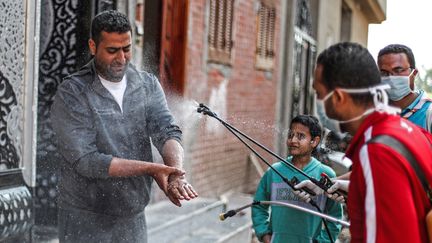 Un volontaire portant un masque vaporise du désinfectant sur un homme, une mesure contre la pandémie de coronavirus, dans le village de Shamma&nbsp;(Egypte), le 1er avril 2020. (MOHAMED EL-SHAHED / AFP)