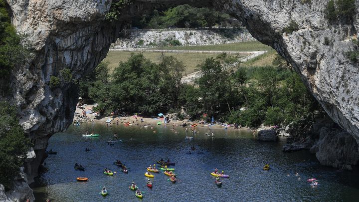 Des personnes naviguent sur des canoës sous le Pont d'Arc dans les Gorges de l'Ardèche, le 1er août 2018. (PHILIPPE DESMAZES / AFP)