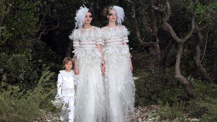 Deux femmes en robe de mari&eacute;e accompagn&eacute;es par un enfant en cl&ocirc;ture du d&eacute;fil&eacute; Chanel, le mardi 22 janvier 2013. (LOIC VENANCE / AFP)