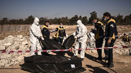 Des membres de la défense civile syrienne des Casques blancs transportent des sacs mortuaires contenant des restes humains retrouvés à Damas, le 16 décembre 2024. (Aris MESSINIS / AFP)