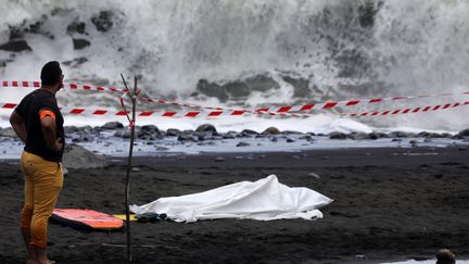 Un policier surveille le corps d'un bodyboardeur tué par un requin, le 21 février 2017, sur une plage de Saint-André, à la Réunion. (RICHARD BOUHET / AFP)