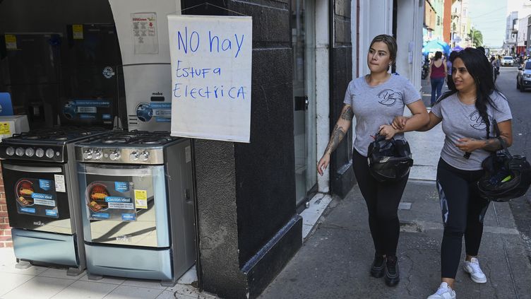 Two people next to a sign explaining that it "there is no electric oven" in an appliance store in Cali (Colombia), while a giant gas cut is underway, May 24, 2023. (JOAQUIN SARMIENTO / AFP)