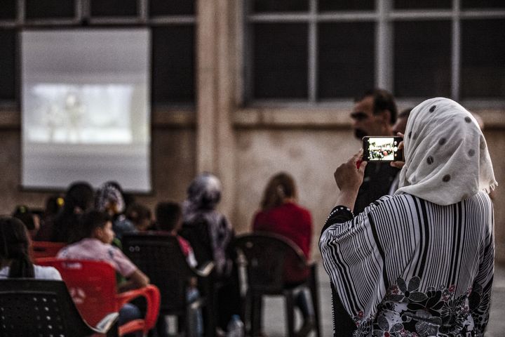 Une femme prend une photo de l'assemblée de spectateurs pendant une séance du cinéma itinérant à Shaghir Bazar, dans le Nord-Est de la Syrie.&nbsp; (DELIL SOULEIMAN / AFP)