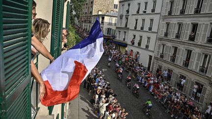 Une Parisienne agite un drapeau à sa fenêtre lors du passage de la course cycliste des Jeux olympiques, dans le quartier de Montmartre, le 4 août 2024. (JULIEN DE ROSA / AFP)