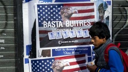 Un jeune garçon passe devant les affiches collées dans les rues de Buenos Aires, où l'on peut aisément voir la critique des fonds dits "vautours" qui réclament le remboursement de la dette argentine. (AFP PHOTO / ALEJANDRO PAGNI)