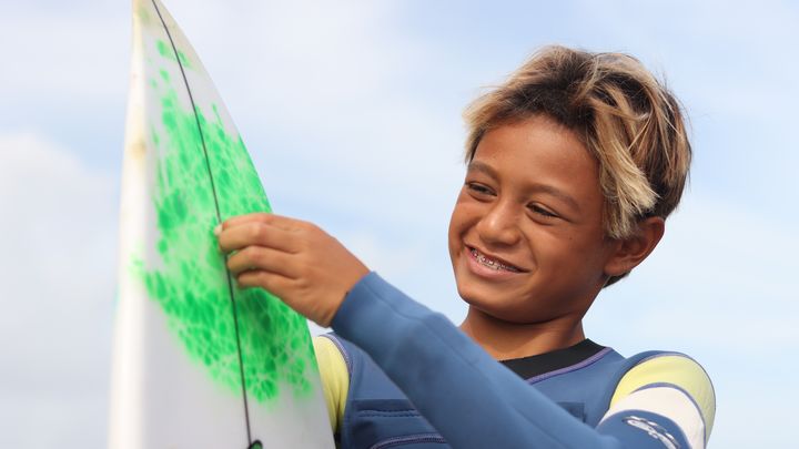 Tauirai, 11 ans, prépare sa planche, le 2 juillet 2024, avant de se mettre à l’eau. (LORRAINE GREGORI / FRANCEINFO: SPORT)