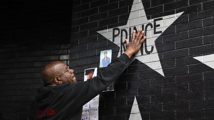 Un fan touche, jeudi 21 avril, le nom de Prince peint sur un des murs de "First Avenue", la boîte de nuit de Minneapolis où a débuté la star. (CRAIG LASSIG / REUTERS)