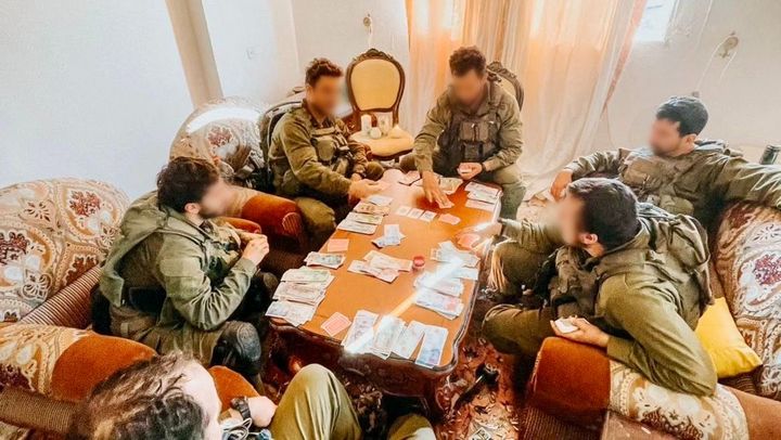 Des soldats israéliens jouent aux cartes avec des liasses de billets, dans une maison. (X / YOUNIS TIRAWI)