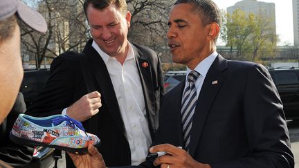 Barack Obama en pleine sc&eacute;ance de d&eacute;dicace de la chaussure d'un supporter. (JEWEL SAMAD / AFP)