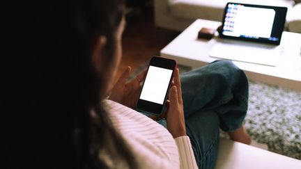 Une femme utilise son téléphone et sa tablette, le 9 avril 2021. (EUGENIO MARONGIU / CULTURA CREATIVE / AFP)