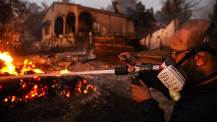 Un homme tente d'éteindre le feu à Vrilissia, dans la banlieue d'Athènes en Grèce, le 12 août. (ARIS OIKONOMOU / AFP)