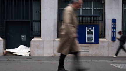 Un homme bien habillé passe devant un SDF dormant devant une porte d'entrée à Paris (JOEL SAGET / AFP)