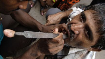 L'assistant d'un dentiste itin&eacute;rant inspecte la dentition d'un patient dans une rue de Varanasi (Inde), le 28 ao&ucirc;t 2012. (AFP)