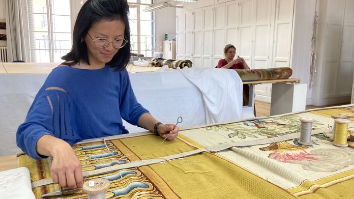 Julienne Tsang, responsable adjointe de l'atelier de restauration de tapis, travaille sur un tapis des années 1960, au Mobilier national, le 30 mai 2023. (MELANIE KUSZELEWICZ / RADIO FRANCE)