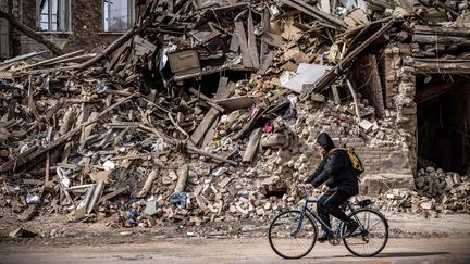 Un homme passe à vélo devant les décombres d'un bâtiment détruit dans la ville de Kharkiv, le 2 avril 2022. Photo d'illustration. (FADEL SENNA / AFP)