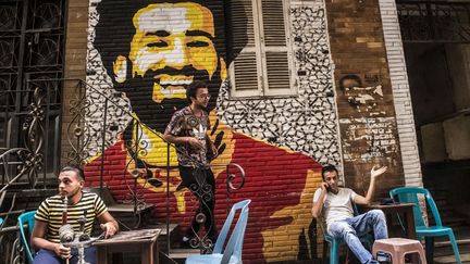 Dans un café en plein air du centre-ville, un artiste égyptien, Ahmed Fathy, descend un petit escalier devant une immense fresque murale. Celle-ci représente le visage souriant du milieu de terrain égyptien de Liverpool Mohamed Salah qui empile les récompenses et est pressenti pour décrocher le prochain Ballon d'or, après Ronaldo et Messi. Issu d'une famille pauvre d'un village du delta du Nil, le parcours de Salah fait rêver de nombreux Egyptiens. Sacré en janvier, «meilleur joueur africain», il a été désigné meilleur joueur de la saison en première ligue en Angleterre, le 22 avril 2018. Au-delà de ses performances en club, il a grandement contribué à la première qualification de l'Egypte en coupe du monde depuis 28 ans. Et ce dribbleur hors pair aux pieds de velours pourrait faire se lever les foules lors du Mondial-2018 en Russie, qui débute le 14 juin 2018. Se tenant éloigné de la scène politique, il soutient néanmoins une campagne de l'ONU en Egypte contre les inégalités et les violences faites aux femmes. Il s'affiche également dans un clip contre la drogue, fléau qui touche les jeunes. (KHALED DESOUKI / AFP)