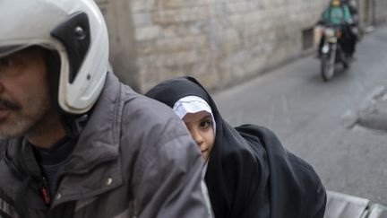 Une écolière et son père, à moto, dans une rue de Téhéran, le 29 janvier 2023. (MORTEZA NIKOUBAZL / NURPHOTO / AFP)