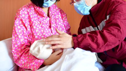 Deux parents vêtus de masques pour lutter contre le nouveau coronavirus enlacent leur nouveau-né à l'hôpital de&nbsp;Taiyuan, dans le nord de la Chine, le 5 février 2020. (CAO YANG / XINHUA / AFP)