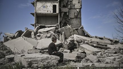 Un jeune garçon assis devant un bâtiment endommagé par une frappe à Kramatorsk, dans la région du Donbass, dans l'est de l'Ukraine, le 25 mai 2022. (ARIS MESSINIS / AFP)