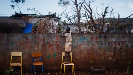 Un enfant regarde la cour de son école, dans le village de Bouyouni (Mayotte), le 19 décembre 2024. Mais les établissements scolaires ne pourront pas tous rouvrir à la rentrée du 13 janvier, a averti Emmanuel Macron, évoquant la possibilité de scolariser certains élèves dans les établissements de La Réunion voisine. (DIMITAR DILKOFF / AFP)