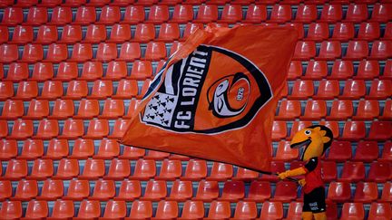 La mascotte du FC Lorient tient un drapeau du club dans une tribune vide, le 21 février 2021. (LOIC VENANCE / AFP)