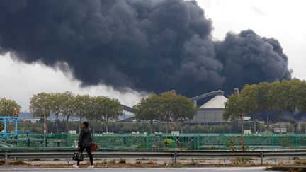 Une passante devant le panache de fumée qui se dégage de l'usine chimique Lubrizol, à Rouen (Seine-Maritime), jeudi 26 septembre. (PASCAL ROSSIGNOL / REUTERS)