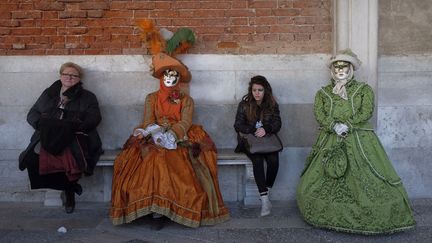 Des touristes partagent un banc avec des participants au carnaval de Venise (Italie) place Saint-Marc, le 23 f&eacute;vrier 2014. (REUTERS)