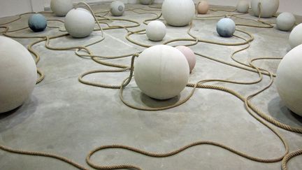 Pour la Biennale, Otobong Nkanga crée une installation composée de boules de béton de différentes dimensions, peintes en bleu et reliées entre elles par des cordages, tandis qu’une bande-son envahit l’espace. 
 (Anne-Sophie Saboureau)