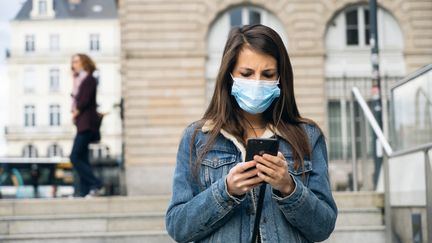 Une femme est penchée sur son téléphone, à Rennes, en avril 2020. (VALENTIN BELLEVILLE / HANS LUCAS / AFP)