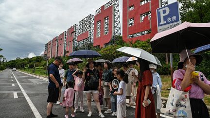 Des habitants attendent le bus devant un panneau : "Un pays, deux systèmes, pour unifier la Chine", le 3 août 2022 à Xiamen (Chine), ville située en face de Taïwan. (HECTOR RETAMAL / AFP)