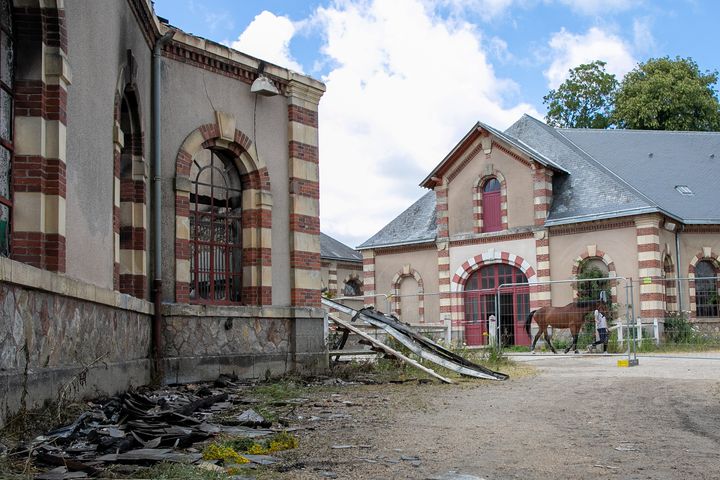 Un homme passe en tenant un cheval devant les bâtiments dévastés du haras national de Saint-Lô. (LOU BENOIST / AFP)