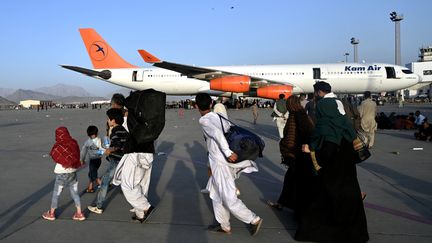 Une famille afghane se dirige vers un avion sur le départ dans l'aéroport de Kaboul le 16 août 2021. (WAKIL KOHSAR / AFP)