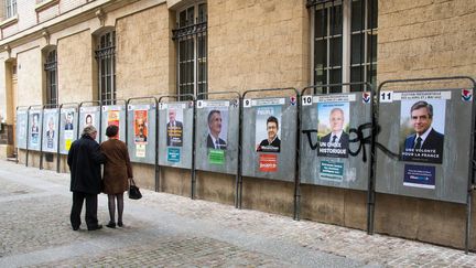 Deux passants devant les affiches de campagne des candidats à l'élection présidentielle, le 10 avril 2017, à Paris. (DANIEL FOURAY / MAXPPP)