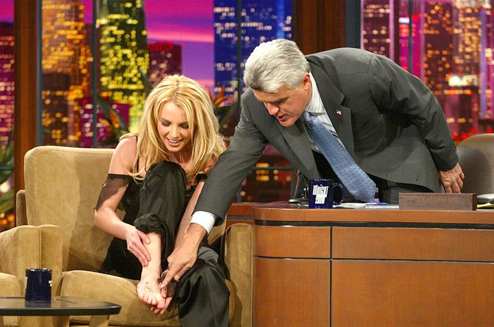 Britney Spears montre un tatouage sur son pied lors de l'émission "The Tonight Show with Jay Leno", le 17 novembre 2003. (KEVIN WINTER / GETTY IMAGES NORTH AMERICA)