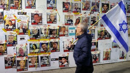 Un home passe avec un drapeau israélien devant des affiches consacrées aux otages enlevés le 7 octobre par le Hamas en Israël, le 16 mars 2024 à Tel-Aviv. (JACK GUEZ / AFP)