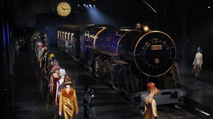 Une gare reconstituée dans la cour carrée du Louvre, une horloge siglée Vuitton et des bruits de pas. Une grille coulisse et dans un halo de fumée apparaît un train bleu. La locomotive siffle, dégageant de la vapeur. Les mannequins -aux talons vertigineux et hauts chapeaux cabossés style 1900- descendent sur le quai-podium, suivies par des petits porteurs aux gants blancs, un bagage dans chaque main. Le train "a été fabriqué rien que pour nous", s'émerveille le styliste :"Nous avons commencé à travailler sur son design il y a cinq mois". Ce "n'est pas un regard nostalgique sur le passé. On avait en tête la notion romantique d'un bel objet à regarder", explique le styliste. La collection tourne autour de "l'idée du voyage". Il a mis en scène des jupes longues sur des pantalons, réchauffées par des manteaux aux larges boutons scintillants ou des redingotes féminines qui s'allongent. Côté matières, il est parti de "trucs plutôt moches, des laines de couvertures aux couleurs et aux motifs douteux. On les a brodés de cristaux et de motifs en plastique plissés" pour leur offrir de la brillance. "J'aime bien l'idée de jouer avec un artisanat humble, ce côté naïf. Ajouter un bouton-bijou sur un manteau camel pour le rendre pimpant, c'est le truc le plus débile qui soit", explique encore le styliste.
 (FRANCOIS GUILLOT / AFP)