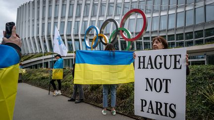 Des Ukrainiens brandissent des drapeaux et pancartes devant le siège du CIO, le 25 mars 2023. (FABRICE COFFRINI / AFP)