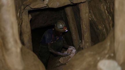 Sans protection et à mains nues, ces creuseurs artisanaux, torche fixée sur le casque, s'engouffrent chaque jour dans des galeries souterraines soutenues par des poutres circulaires.&nbsp; (GUERCHOM NDEBO / AFP)