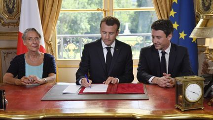 Emmanuel Macron signe le projet de loi de réforme de la SNCF, entouré de la ministre des transports,&nbsp;Elisabeth Borne, et du porte-parole du gouvernement,&nbsp;Benjamin Griveaux, le 27 juillet 2018, au palais de l'Elysée, à Paris.&nbsp; (JULIEN DE ROSA / AFP)