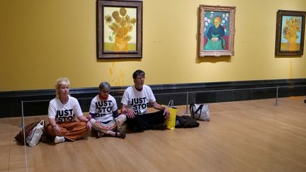 Une photo distribuée par le groupe de campagne climatique Just Stop Oil montre trois activistes assis sur le sol sous les "Tournesols" de Vincent Van Gogh après avoir jeté de la soupe à la tomate sur deux tableaux à la National Gallery, dans le centre de Londres, le 27 septembre 2024. (JUST STOP OIL / AFP)