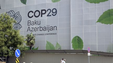 Des personnes passent devant un bâtiment en cours de rénovation, avec une publicité pour la COP29, le 11 septembre 2024 à Bakou (Azerbaïdjan). (TOFIK BABAYEV / AFP)