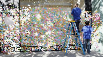 Des employ&eacute;s d'un Apple Store &agrave; Palo Alto (Californie) enl&egrave;vent les post-it de condol&eacute;ances affich&eacute;s sur la vitrine apr&egrave;s l'annonce de la mort de Steve Jobs, le 19 octobre 2011.&nbsp; (KIMIHIRO HOSHINO / AFP)