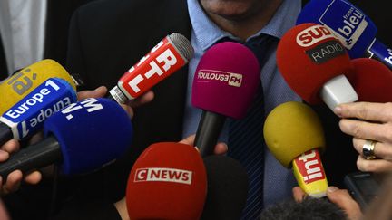 Des micros tenus par des journalistes en train d'interviewer un homme. (PASCAL PAVANI / AFP)