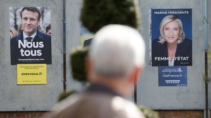 Un homme passe devant les affiches de campagne d'Emmanuel Macron et de Marine Le Pen, le 11 avril 2022 à Denain (Nord). (LUDOVIC MARIN / AFP)